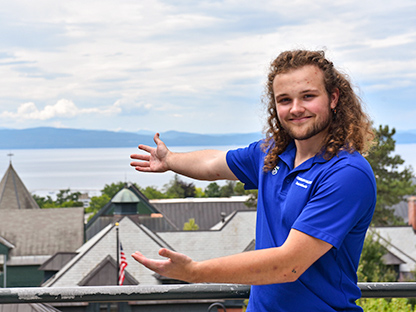 student in blue student ambassador shirt gestures at the beautiful Champlain scenery
