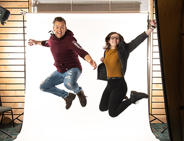 Two students jumping joyfully in front of a white photo background in a studio