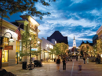Beautiful street shot of Church Street marketplace, lit up at sunset with church steeple glowing white at far end

