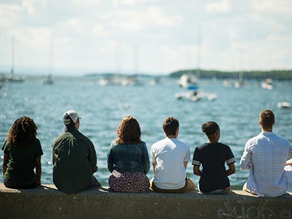 Students from Champlain College in Burlington, Vermont, sitting looking out at Lake Champlain on a sunny summer day

