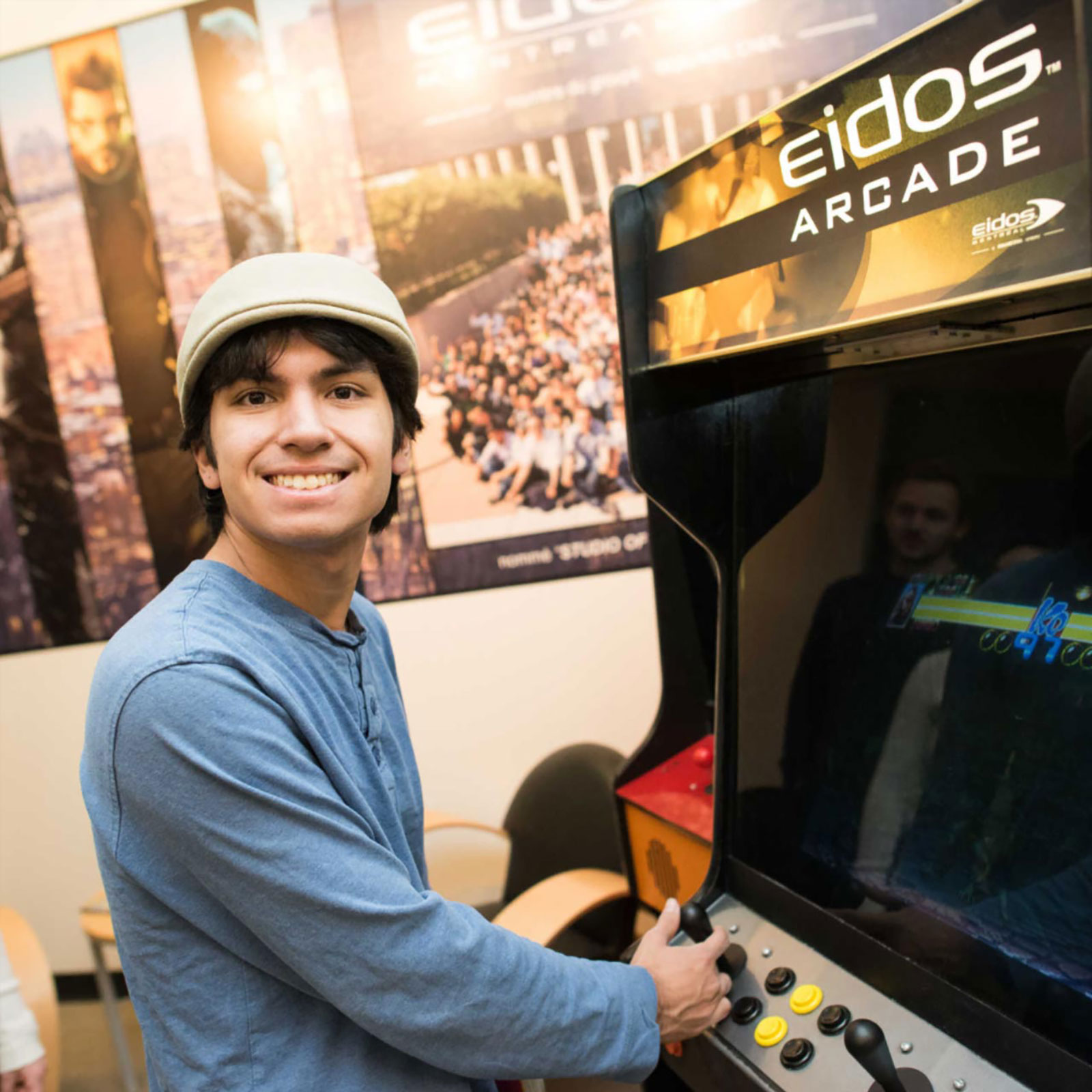 A student playing an arcade game, looking towards the camera and smiling.