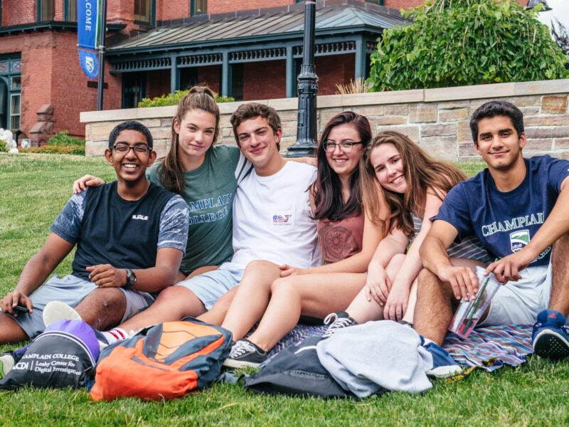 group of students sit on a blanket on the lawn