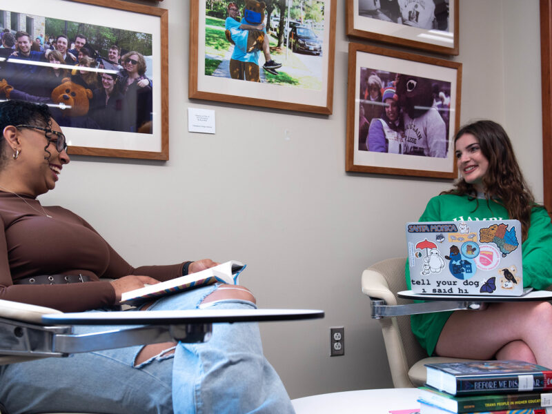 Two students talking while studying in front of several pictures of the Chauncey beaver mascot on a wall