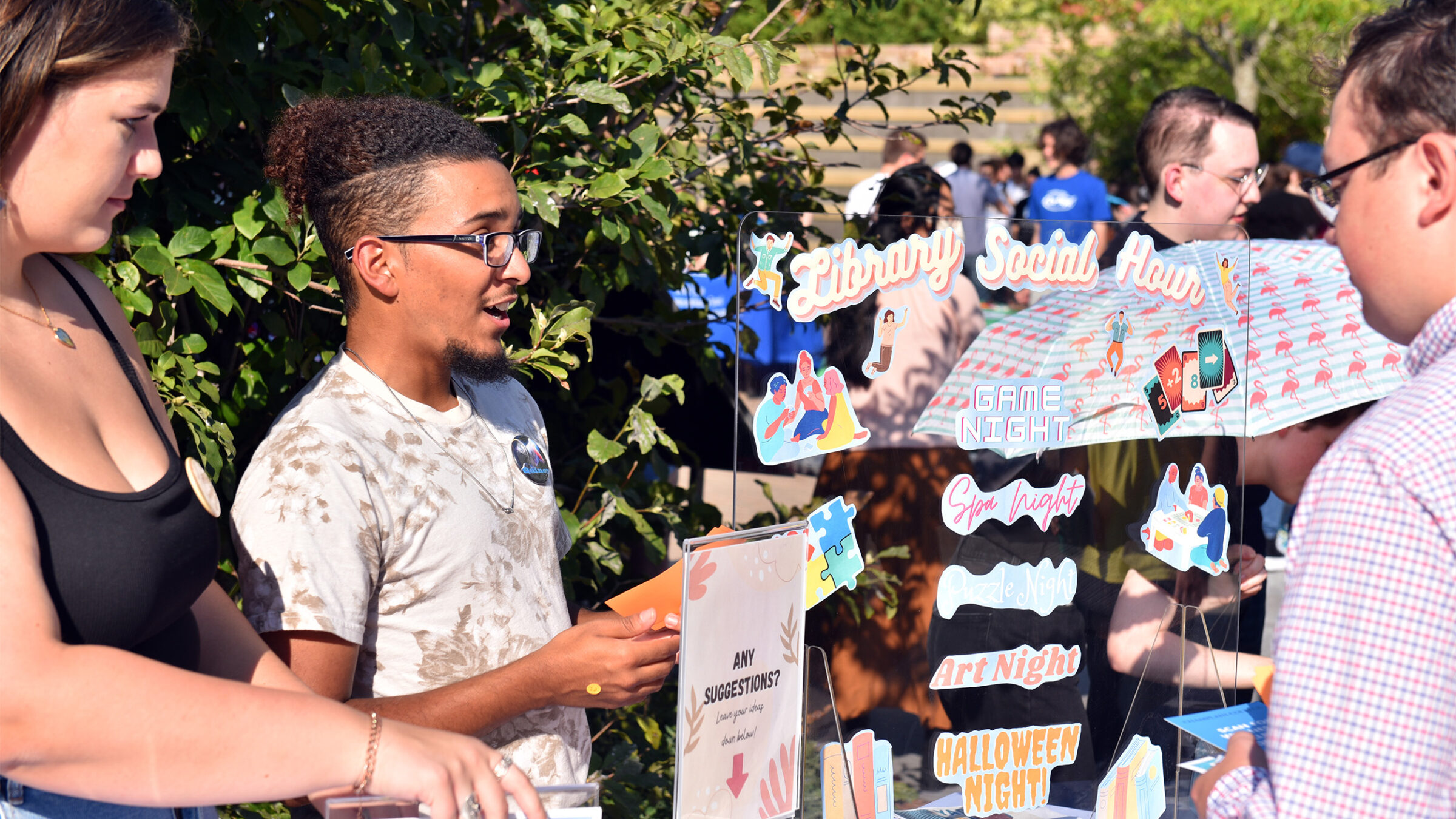 Two students speak with a third about library social hour at an outdoor activities fair