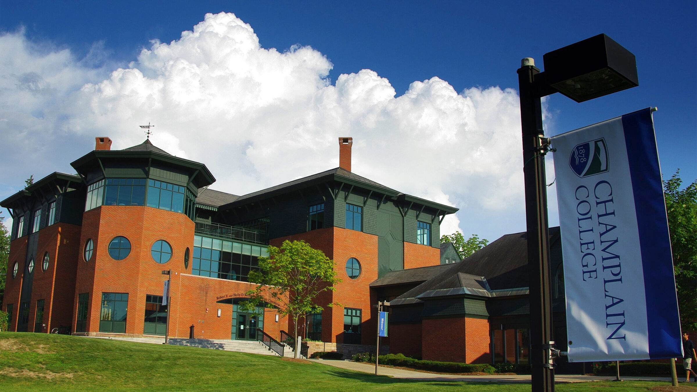 View of quad-side of the Miller Information Commons on a partly cloudy day. A Champlain College banner on a light pole is in the foreground.