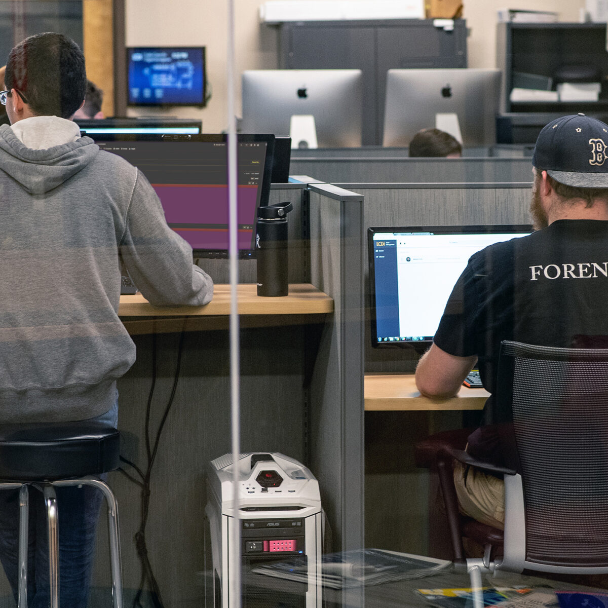students facing computers; "forensics" on the back of student t-shirt