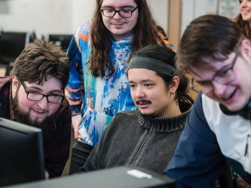 A group of Game Business students collaborating around a computer