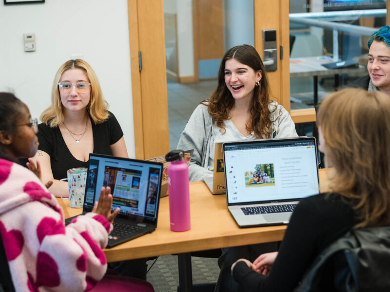 a small group of students having an engaging meeting around a table with their laptops