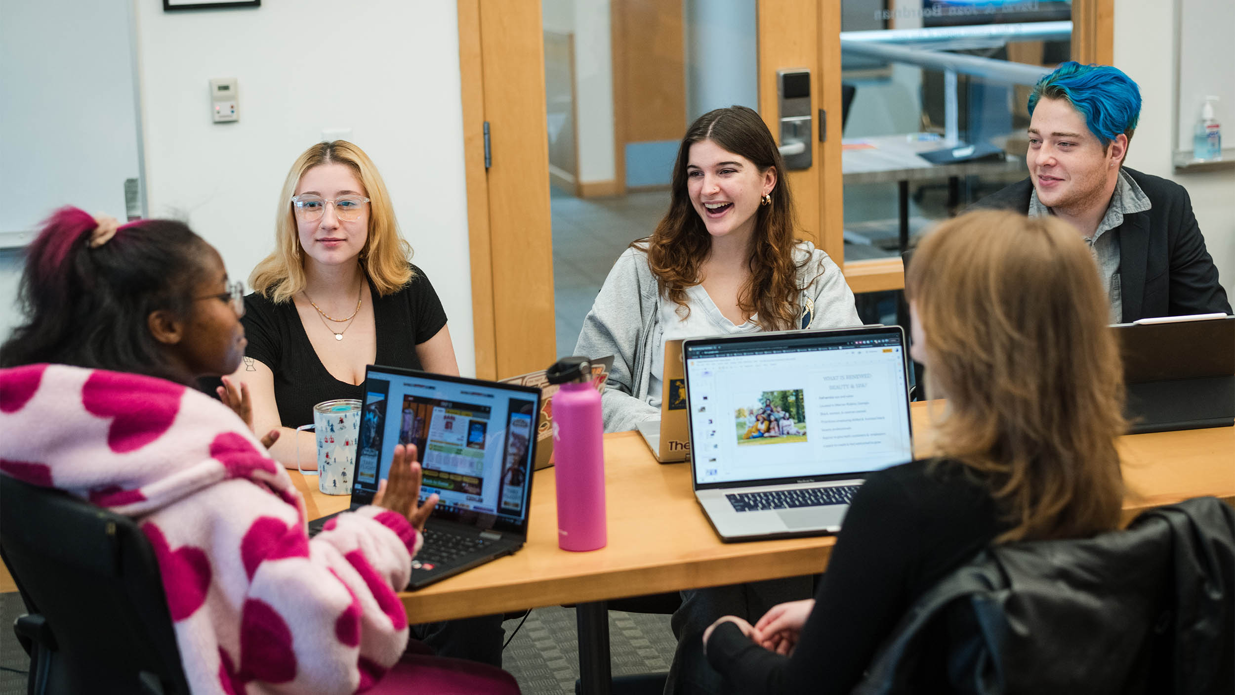 a small group of students having an engaging meeting around a table with their laptops