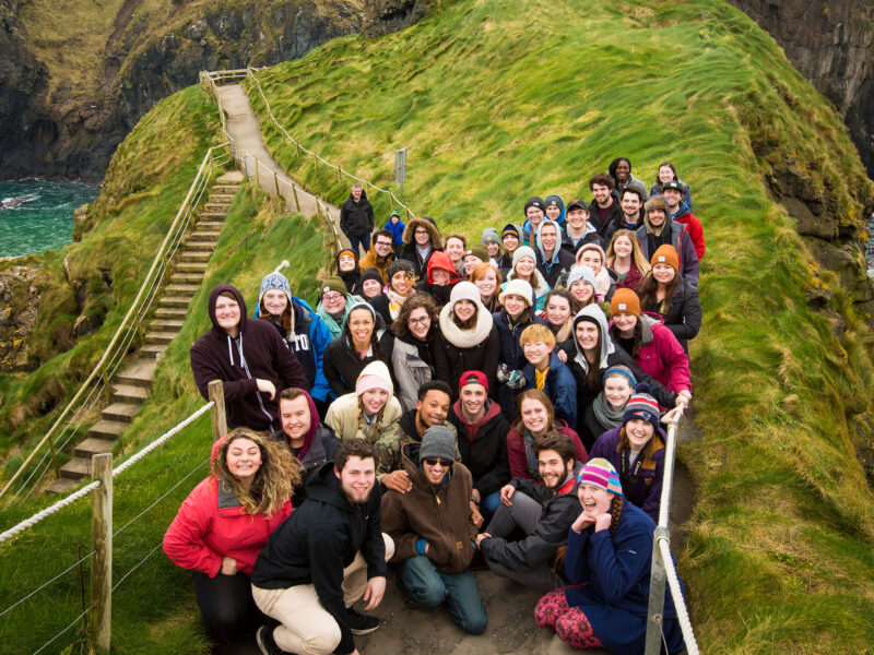 a large group of abroad students gather for a group photo on the cliffs of northern ireland