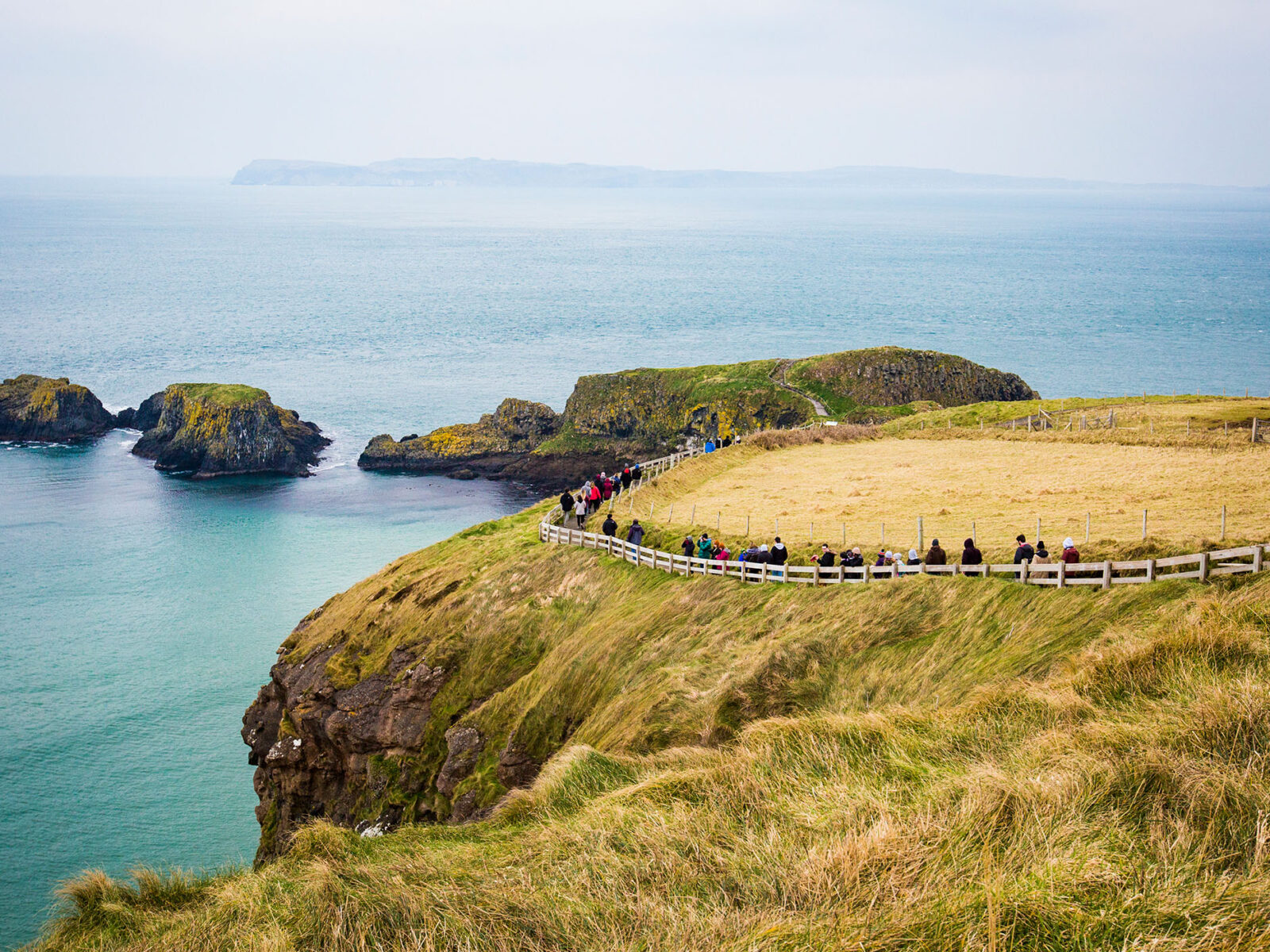 a group of students and tourists walking a path along a cliff side in northern ireland