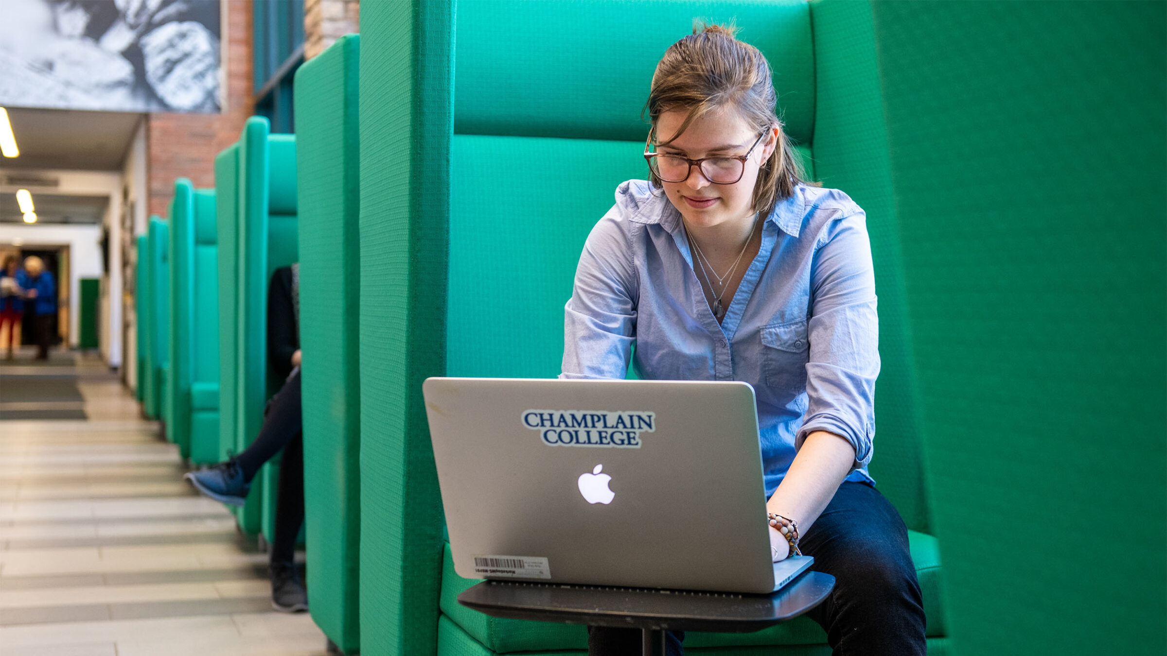 A student in CCM working on their laptop in a green chair