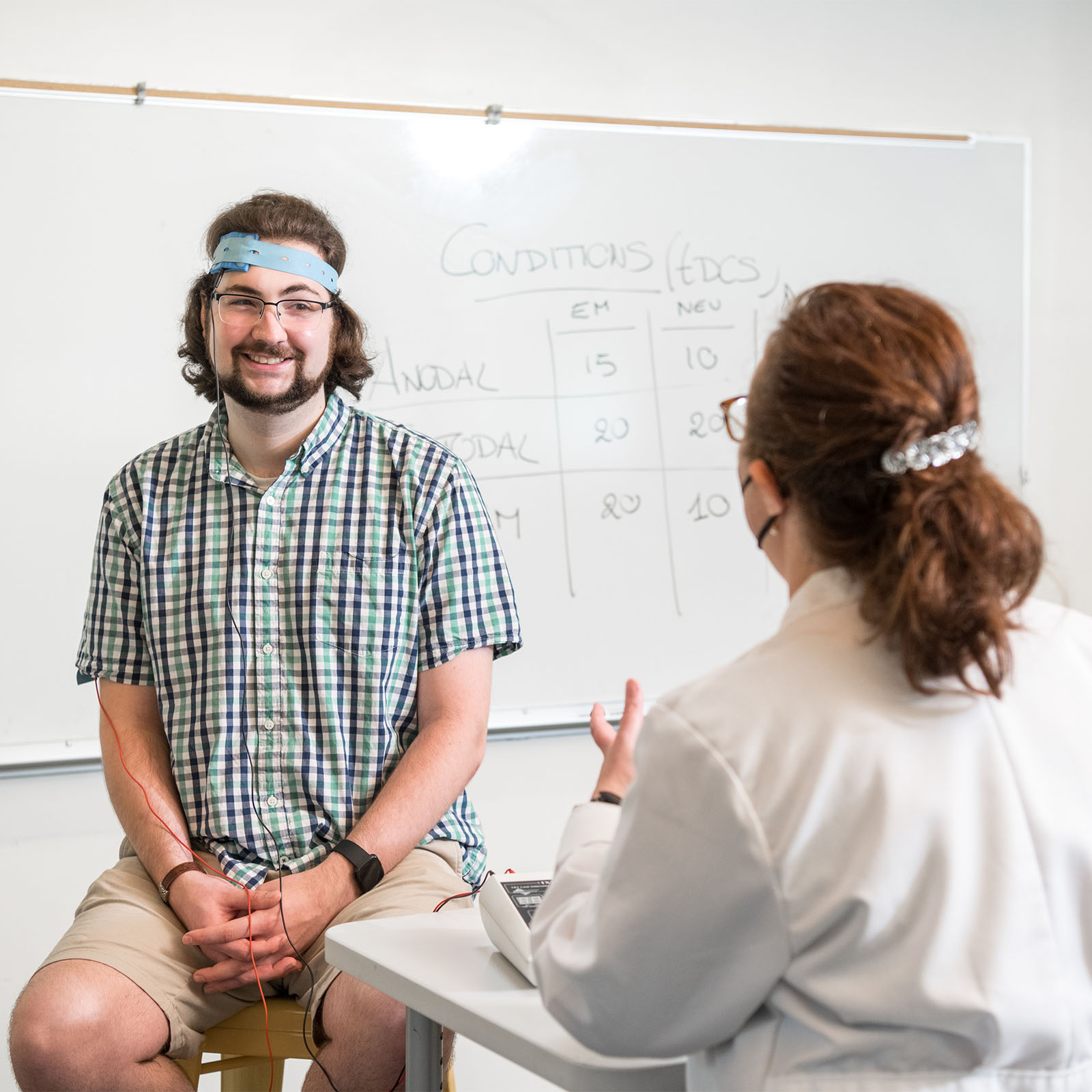 a psychology student wearing headgear and communicating with a professor as part of a study in the neuroscience lab
