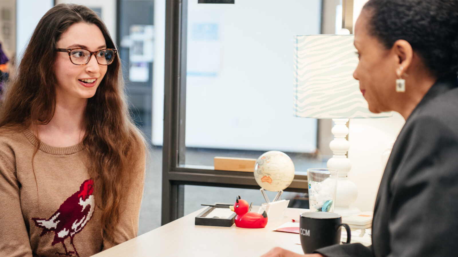 a young woman sits across the desk from an advisor