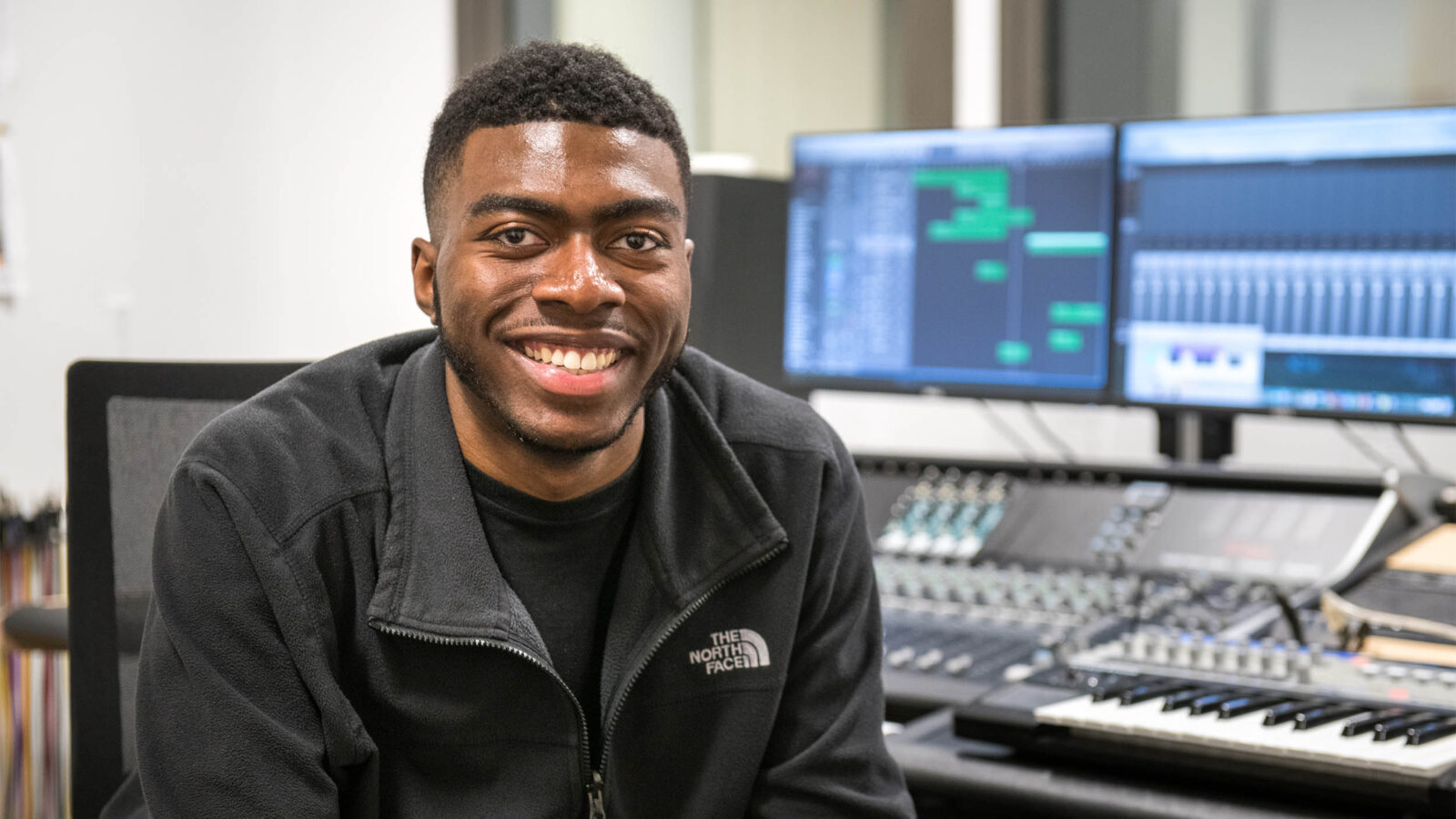 student smiles while sitting near a sound board