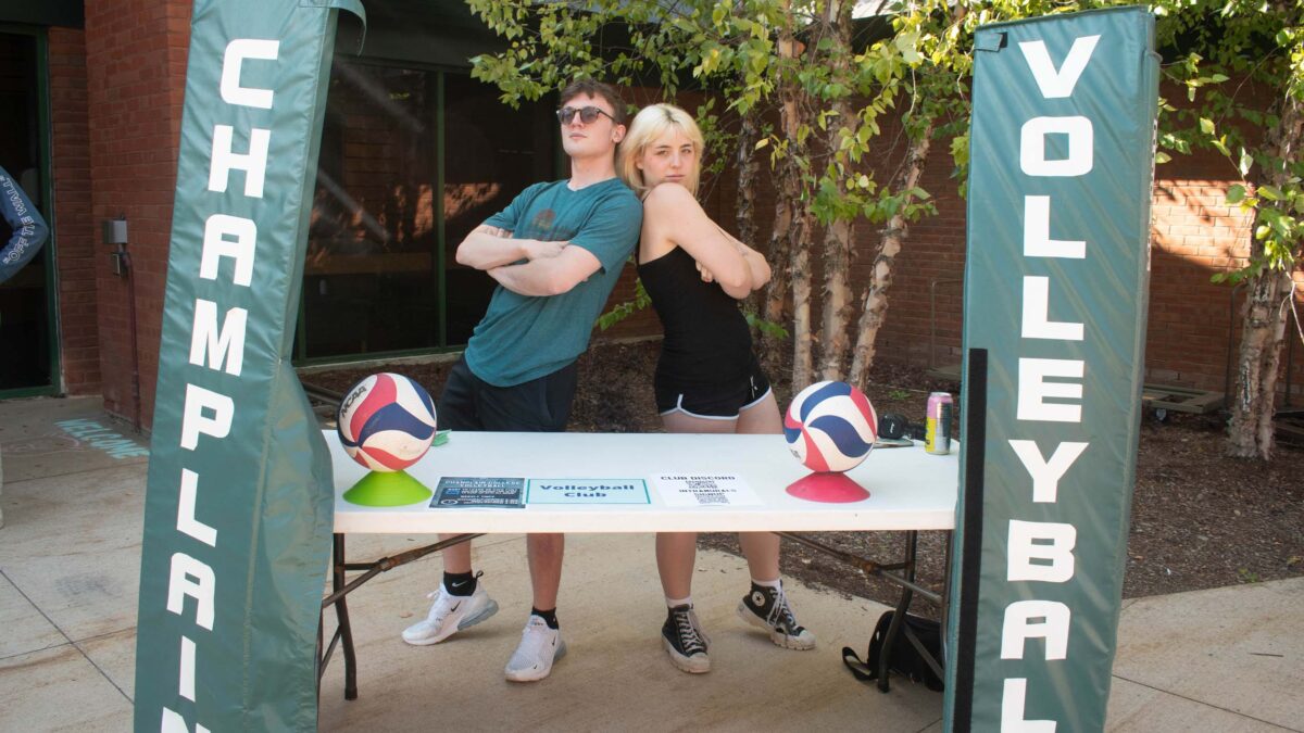 students posing for a photo behind the Champlain volleyball club table at the activities fair