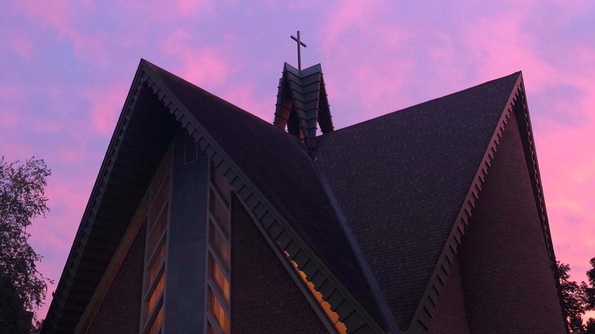 A church with a pink and purple sunset behind it