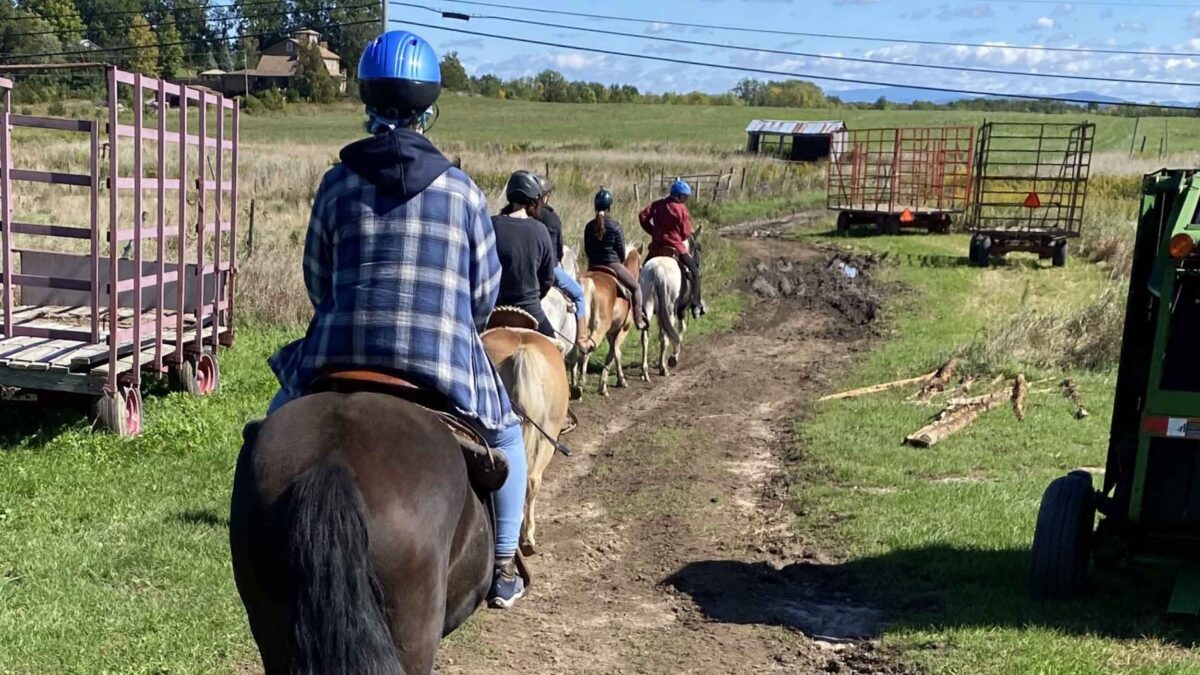 students riding horses in a single file line in the Vermont countryside