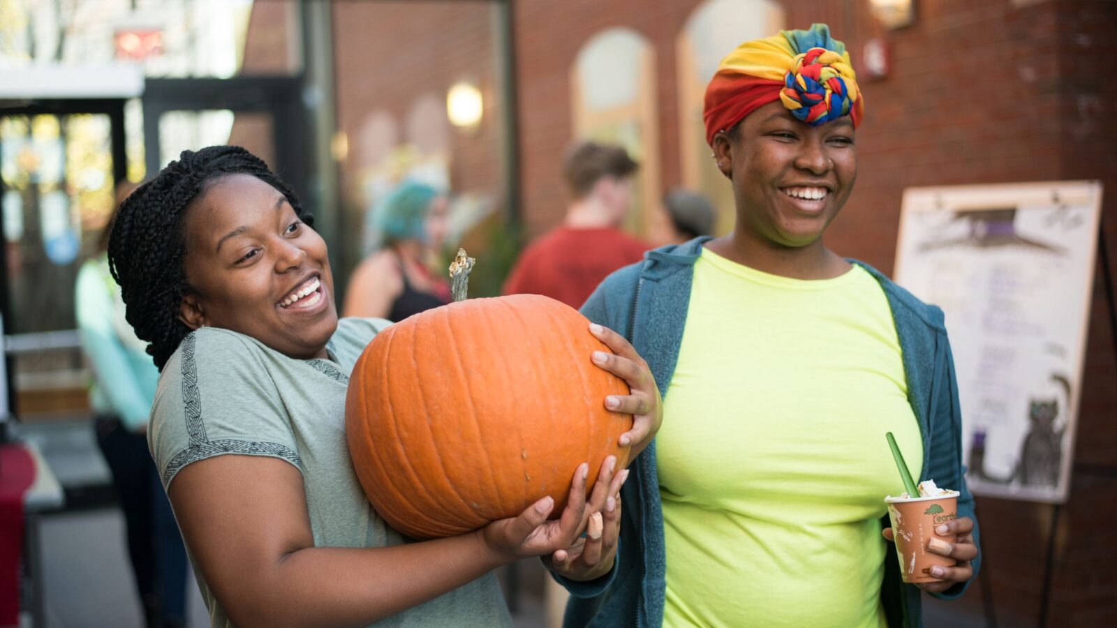 two students stand in IDX with a pumpkin smiling