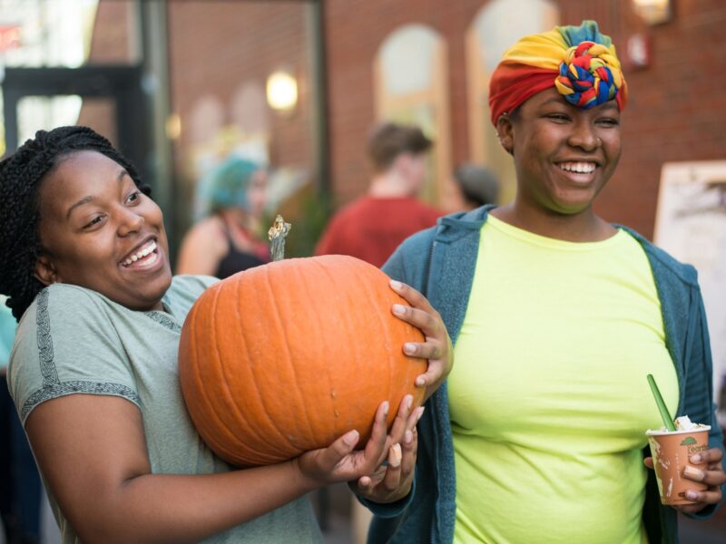 two students stand in IDX with a pumpkin smiling