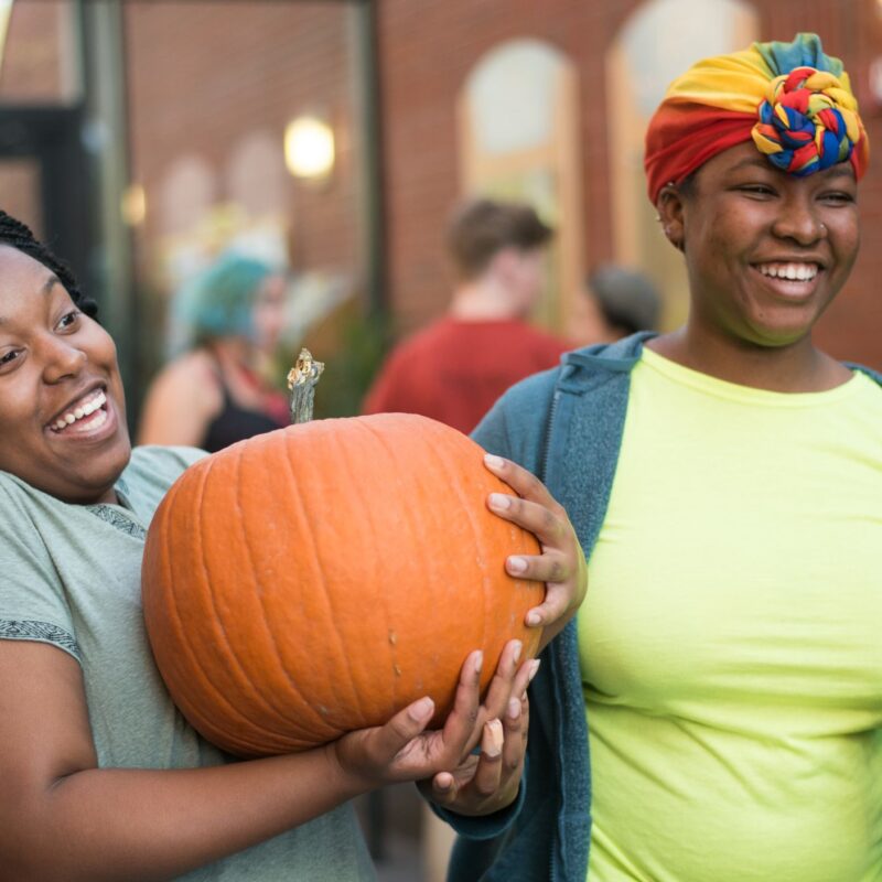 two students stand in IDX with a pumpkin smiling