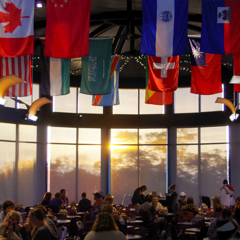 multicultural flags hang above the lively dining hall during sunset