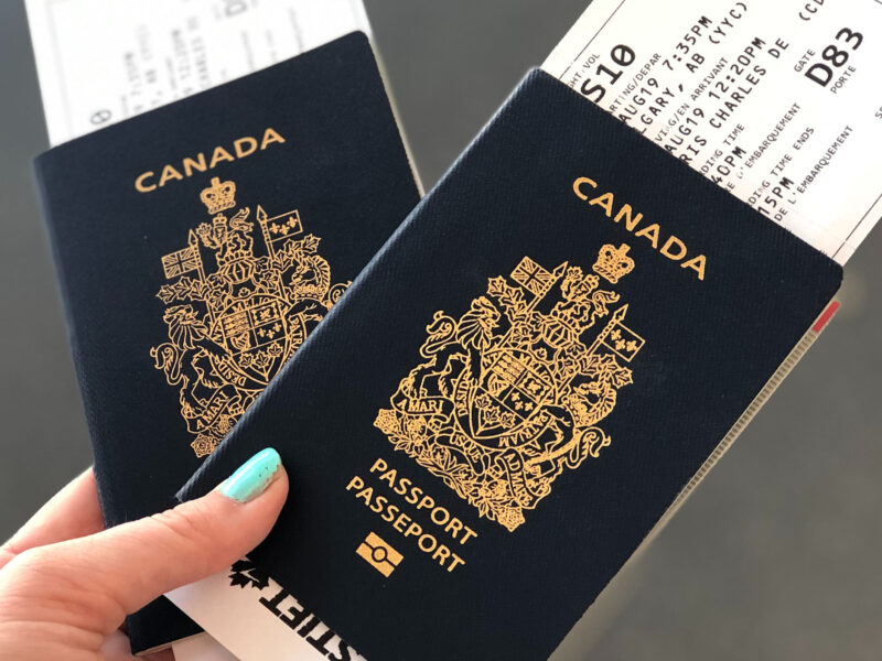 hand holding two canadian passports with plane tickets
