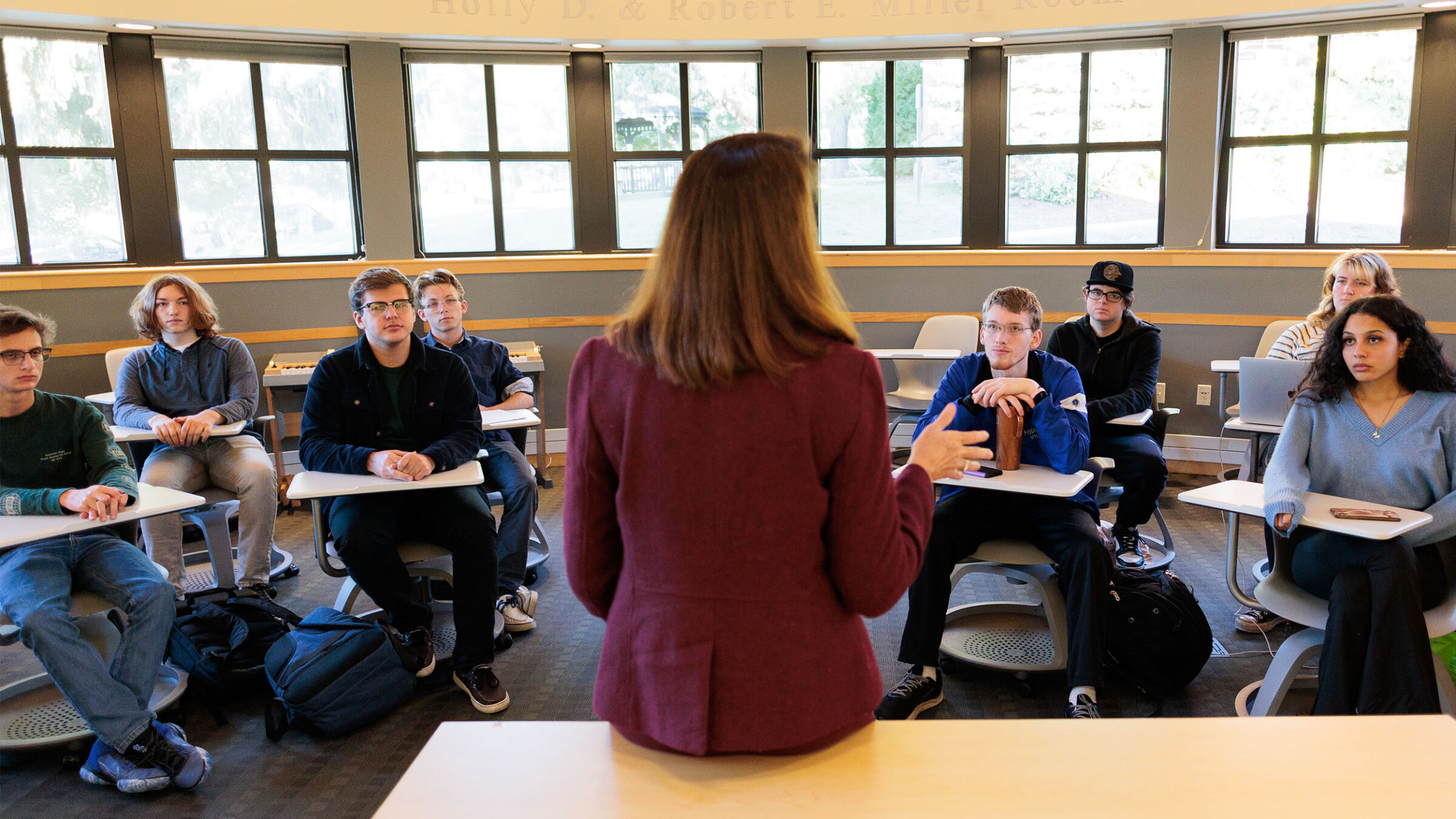 professor at the front of a classroom, delivering a lecture to her students