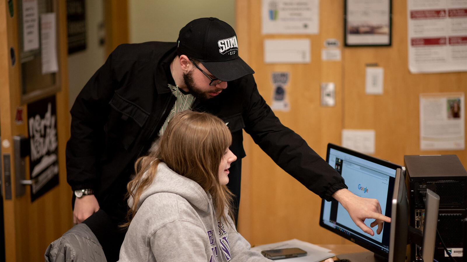 teacher assisting a cybersecurity student who is using a computer