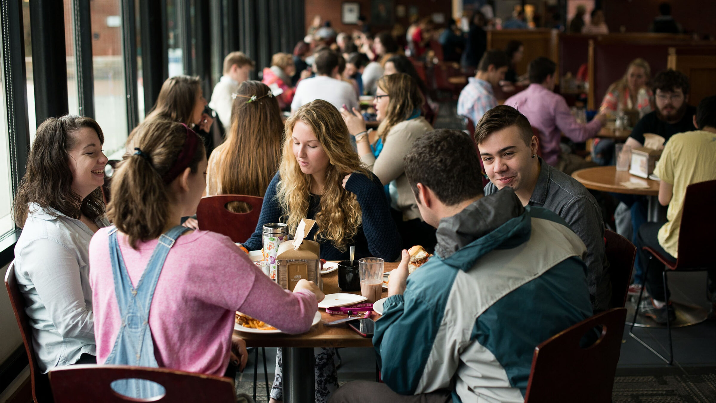 a group of students sitting around a table in the dining hall eating and talking