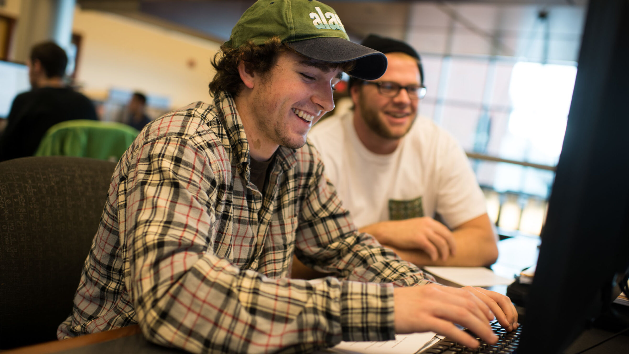 Male student typing on a computer while another watches over his shoulder