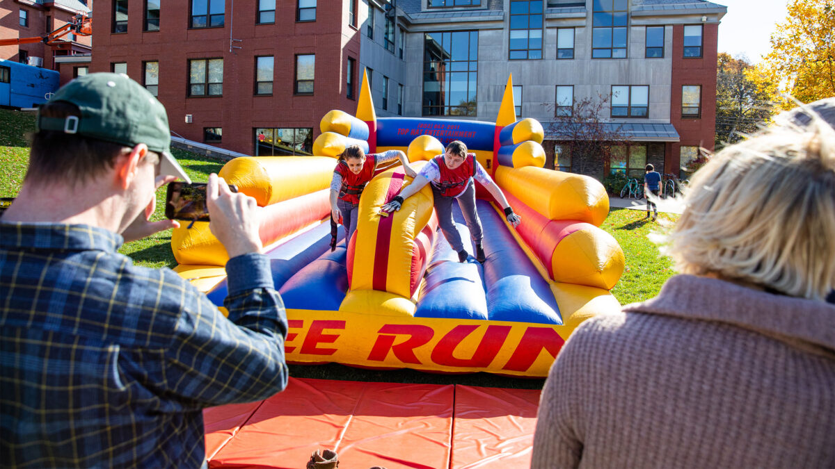 two students compete against each other on an inflatable Bunjee Run game while their parents watch, at the Champlain Weekend event