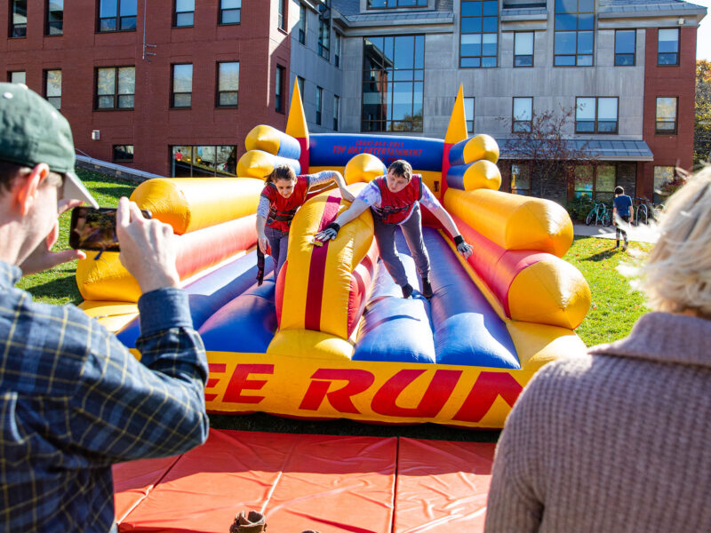 two students compete against each other on an inflatable Bunjee Run game while their parents watch, at the Champlain Weekend event