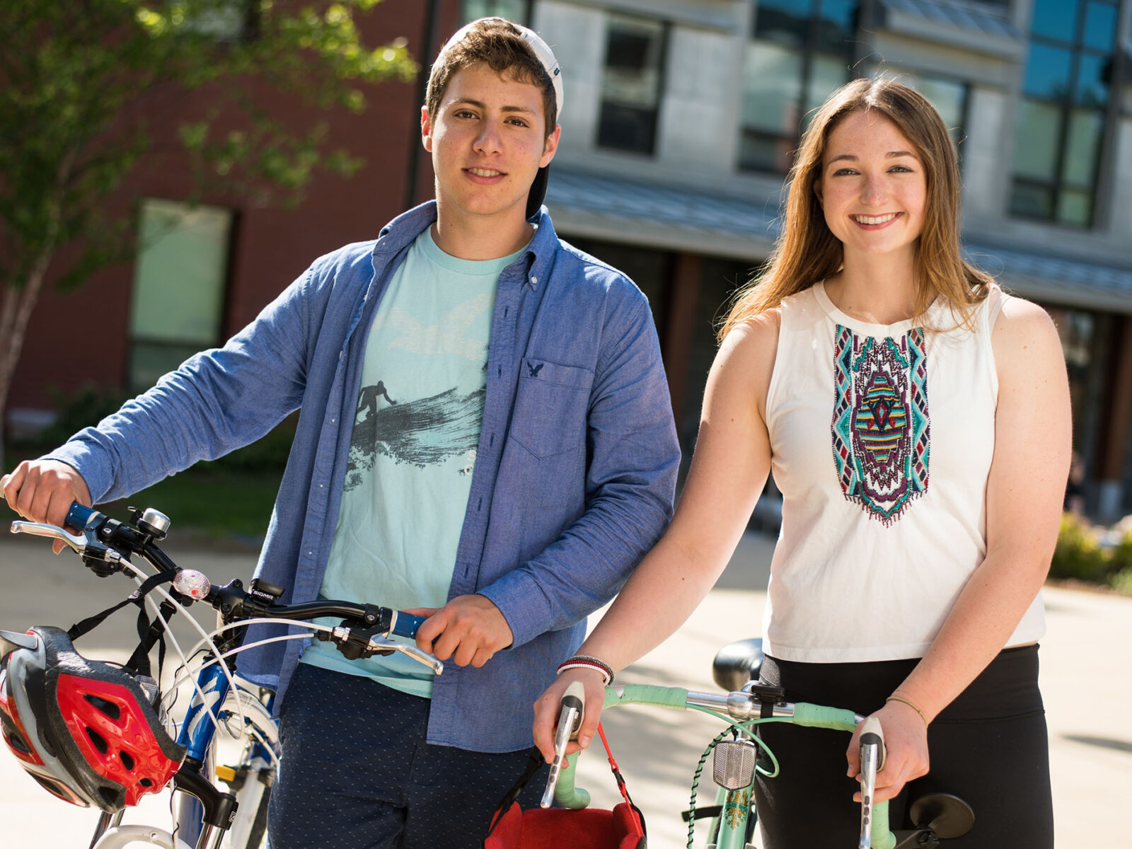 two students walking through campus with their bikes and smiling