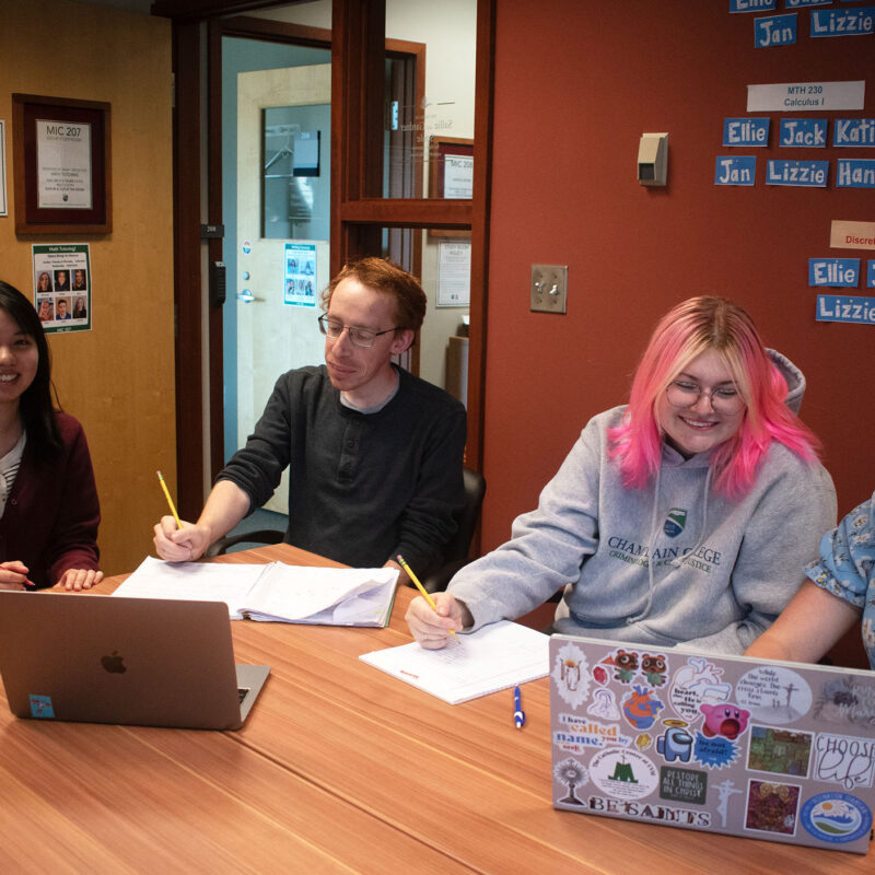 four students sit at laptops in a conference room while studying and receiving peer mentorship