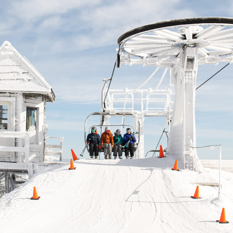 four people on the chair of a ski lift