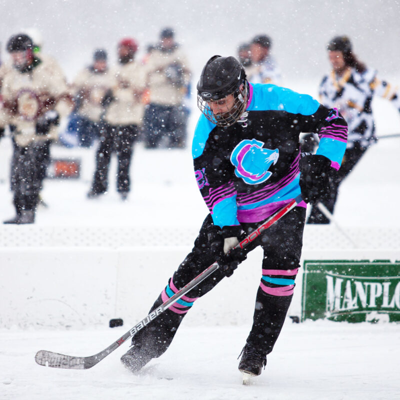 A hockey player takes a shot with the puck during a game played on a frozen lake.