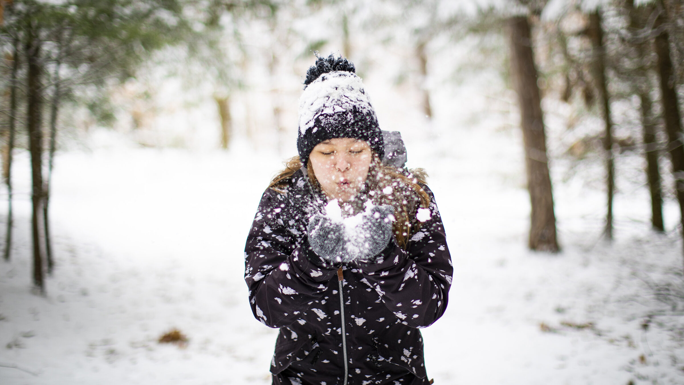 and young woman hold snow in her hands and blows the snowflakes toward the camera