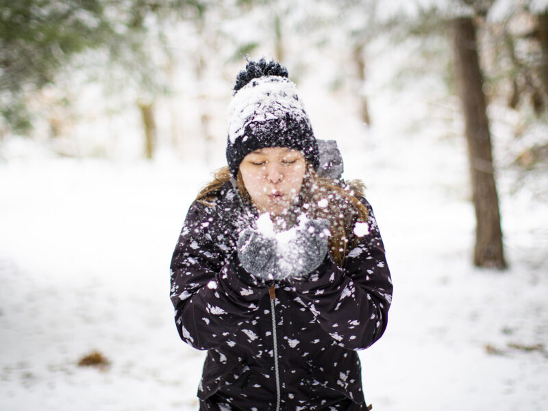 and young woman hold snow in her hands and blows the snowflakes toward the camera