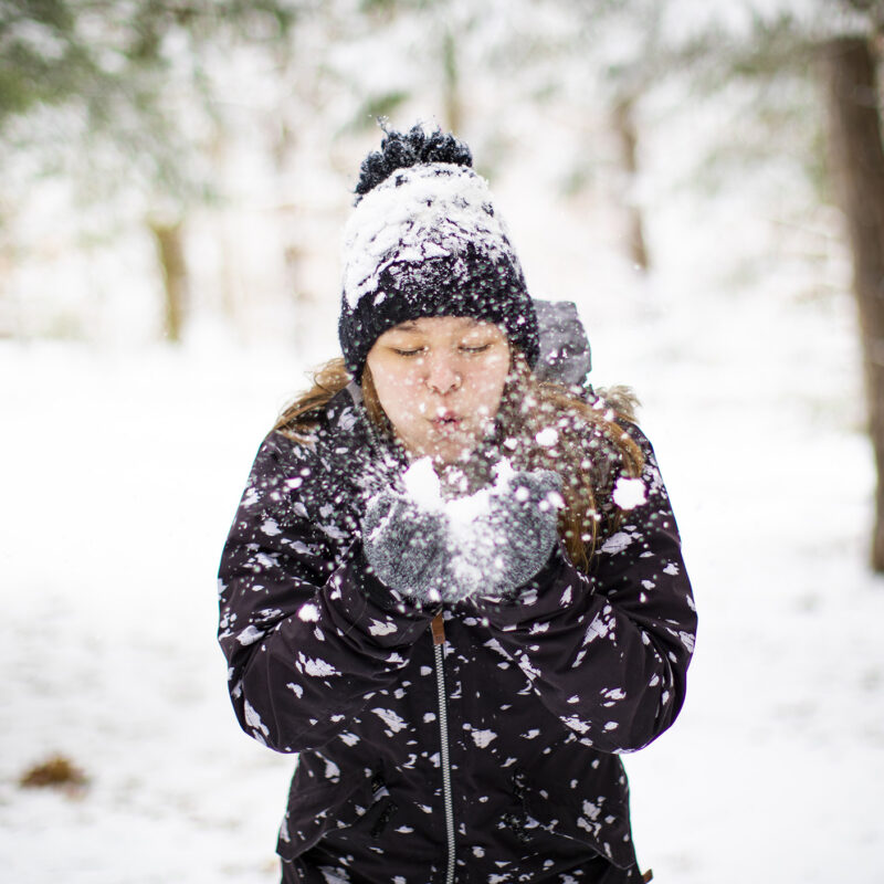 and young woman hold snow in her hands and blows the snowflakes toward the camera