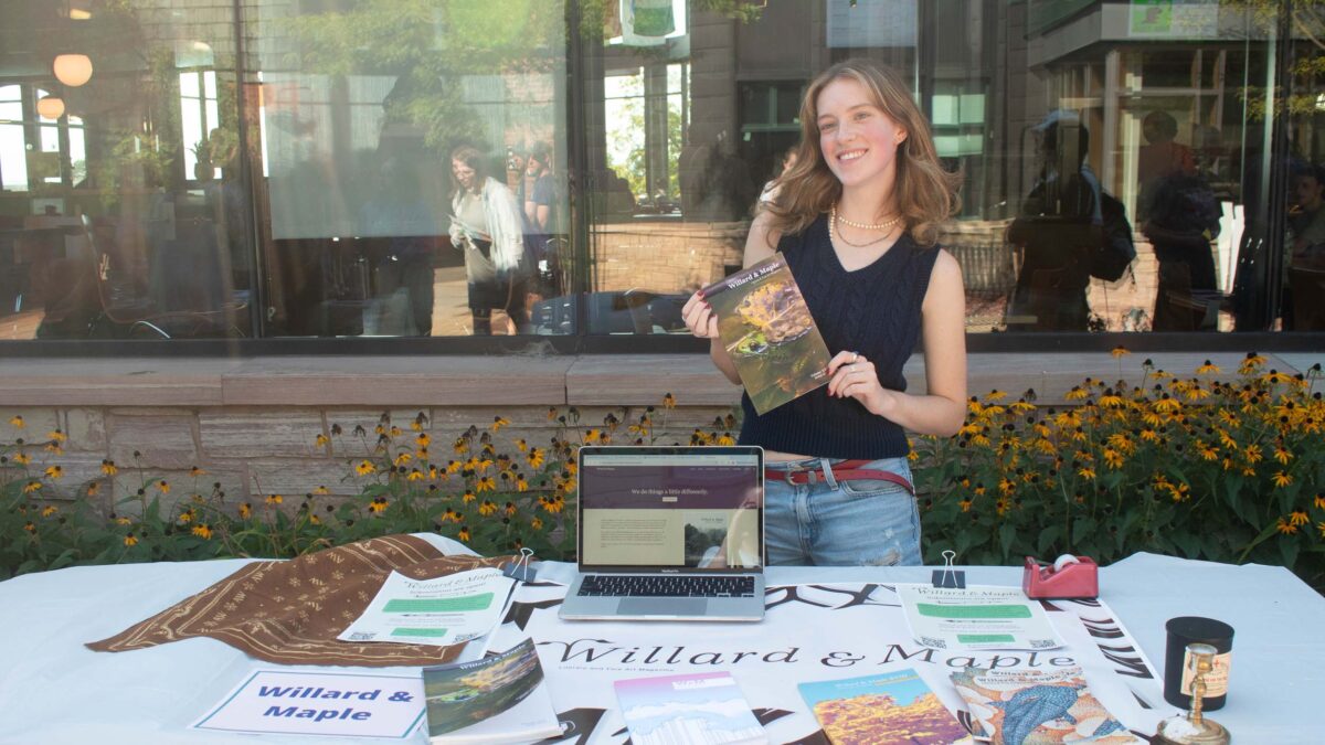 Willard & Maple's student publication tabling at the activity fair with their logo, publications, and laptop