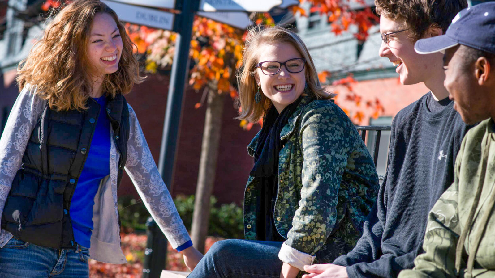 a group of students sitting outside in the fall smiling at each other