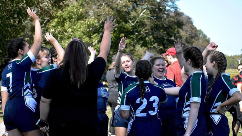 Women's Rugby team huddling with their arms in the air