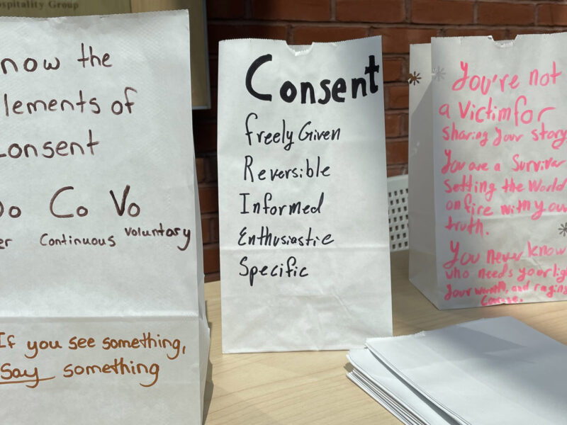three white luminary bags sit on a table with messages about consent and what it means to be a survivor