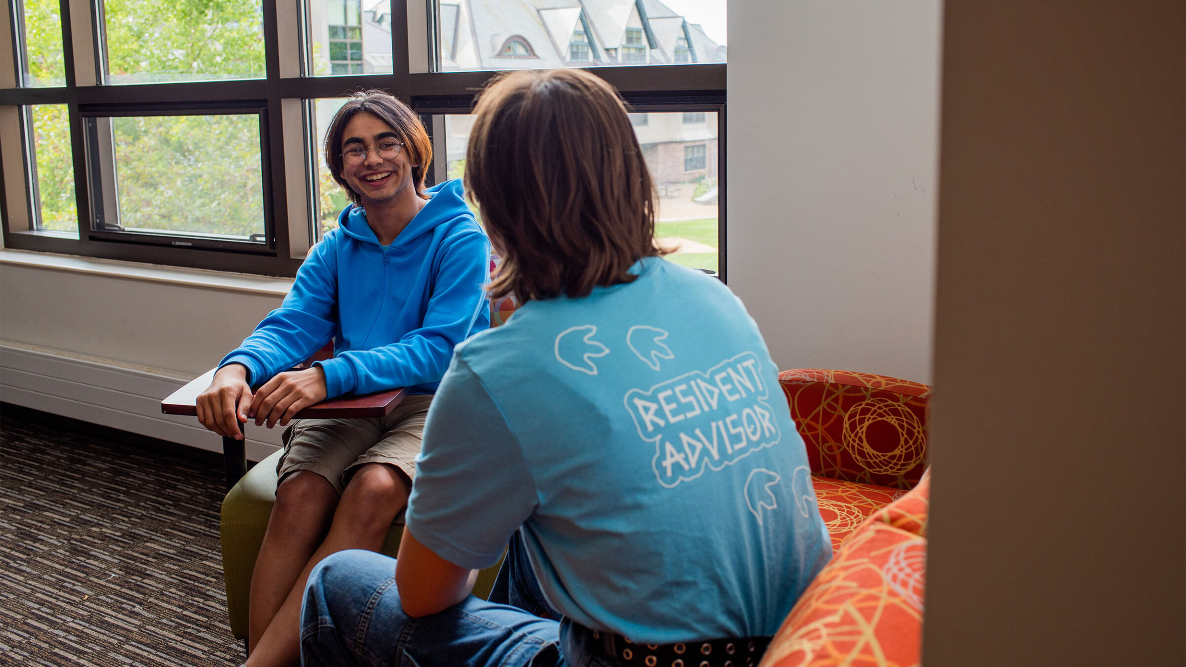 student resident advisor converses with a student in a resident hall lounge space