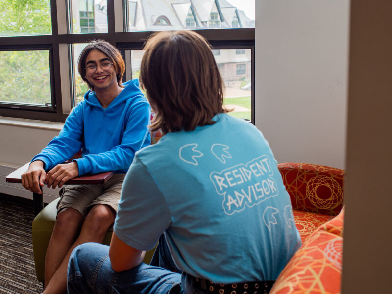 student resident advisor converses with a student in a resident hall lounge space