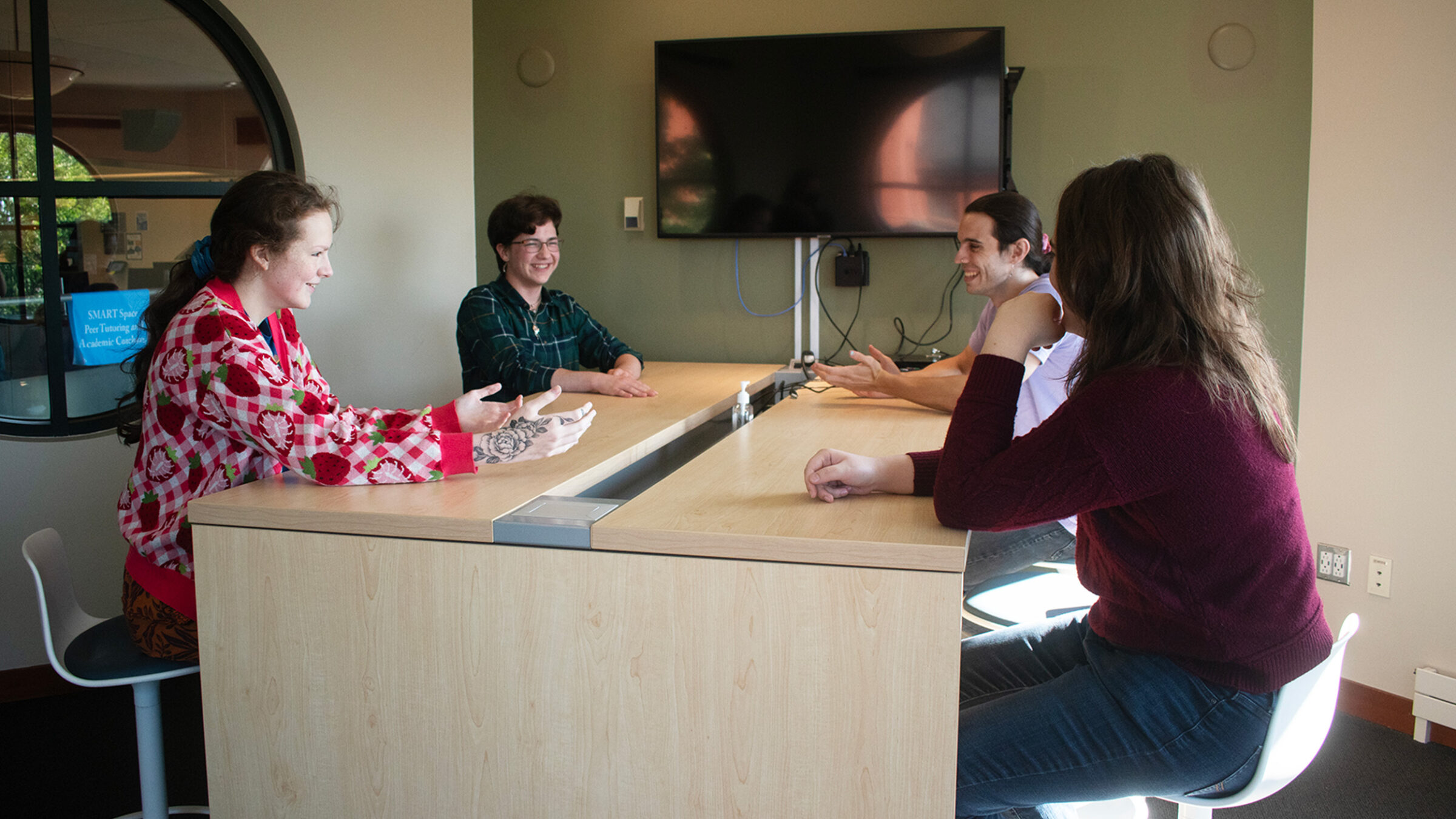 Four students sit around a table talking and laughing on the second floor of the library.