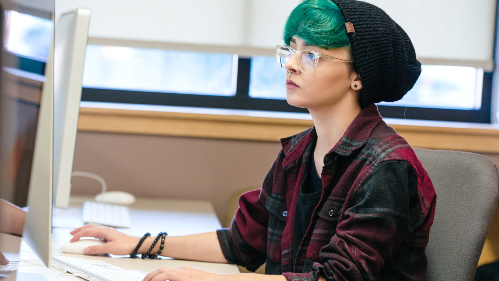 a student with colorful hair works intently at a computer