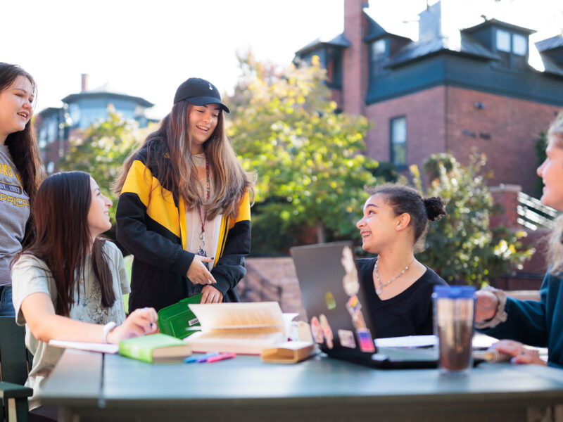 several students gather outside at a table with study materials