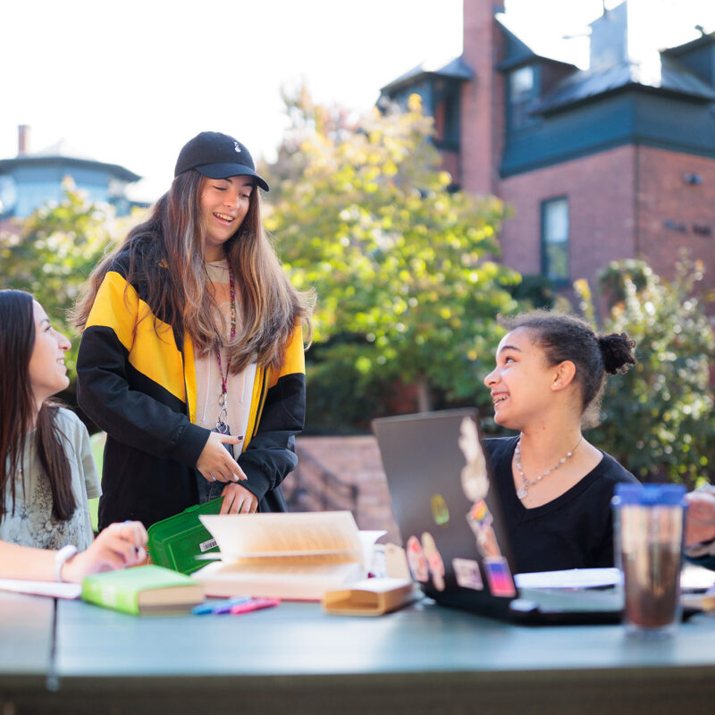 several students gather outside at a table with study materials